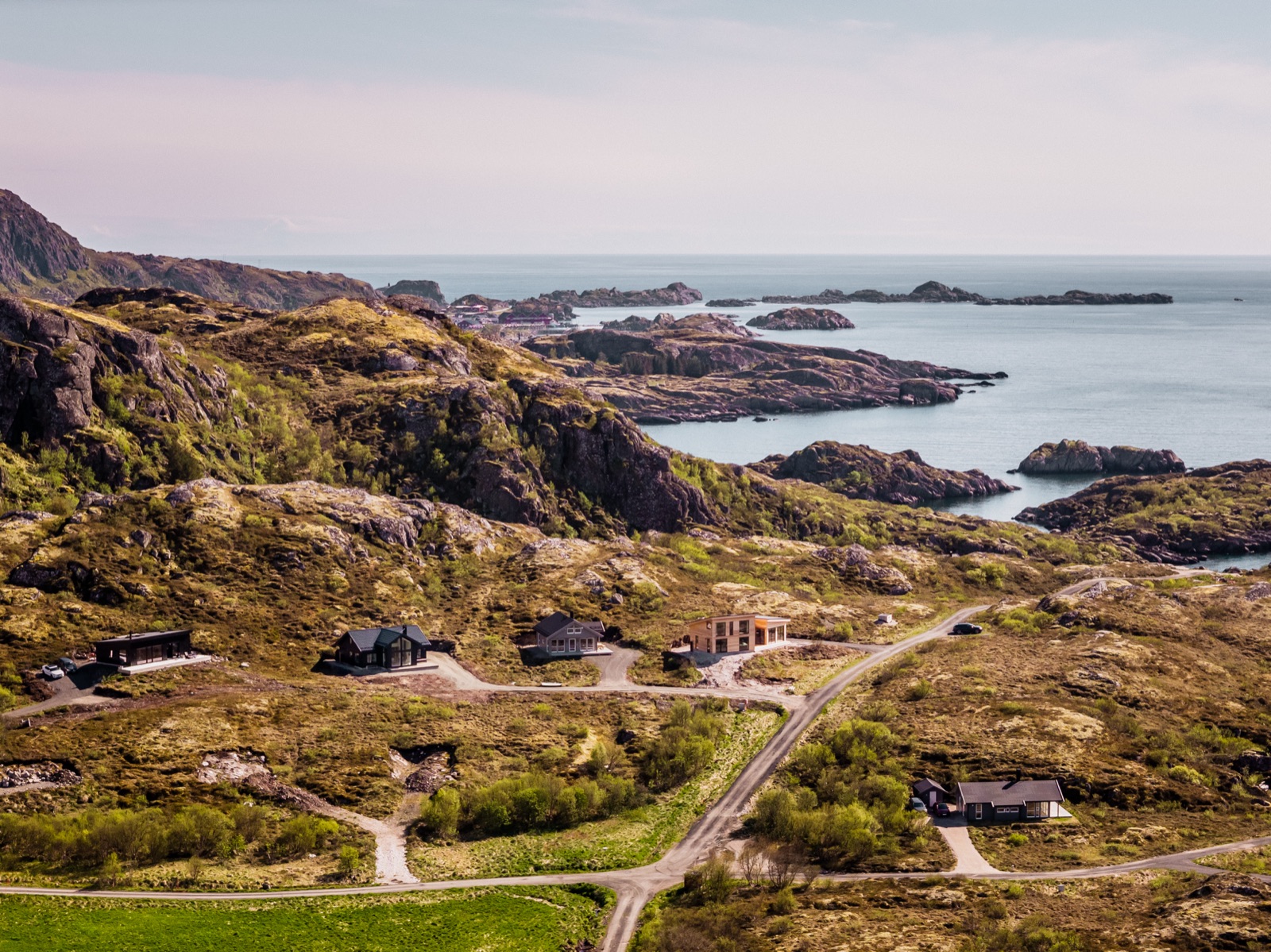 Drone view over the black timber chalet, the fjord, islets and mountains beyond