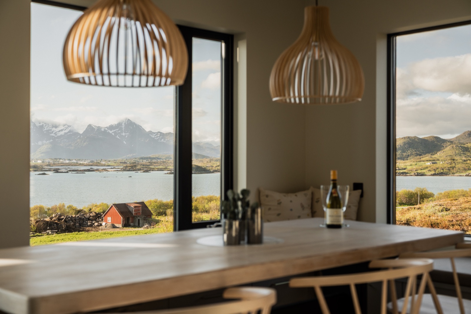 Dining table set with wine glasses, the red barn and fjord through the window behind